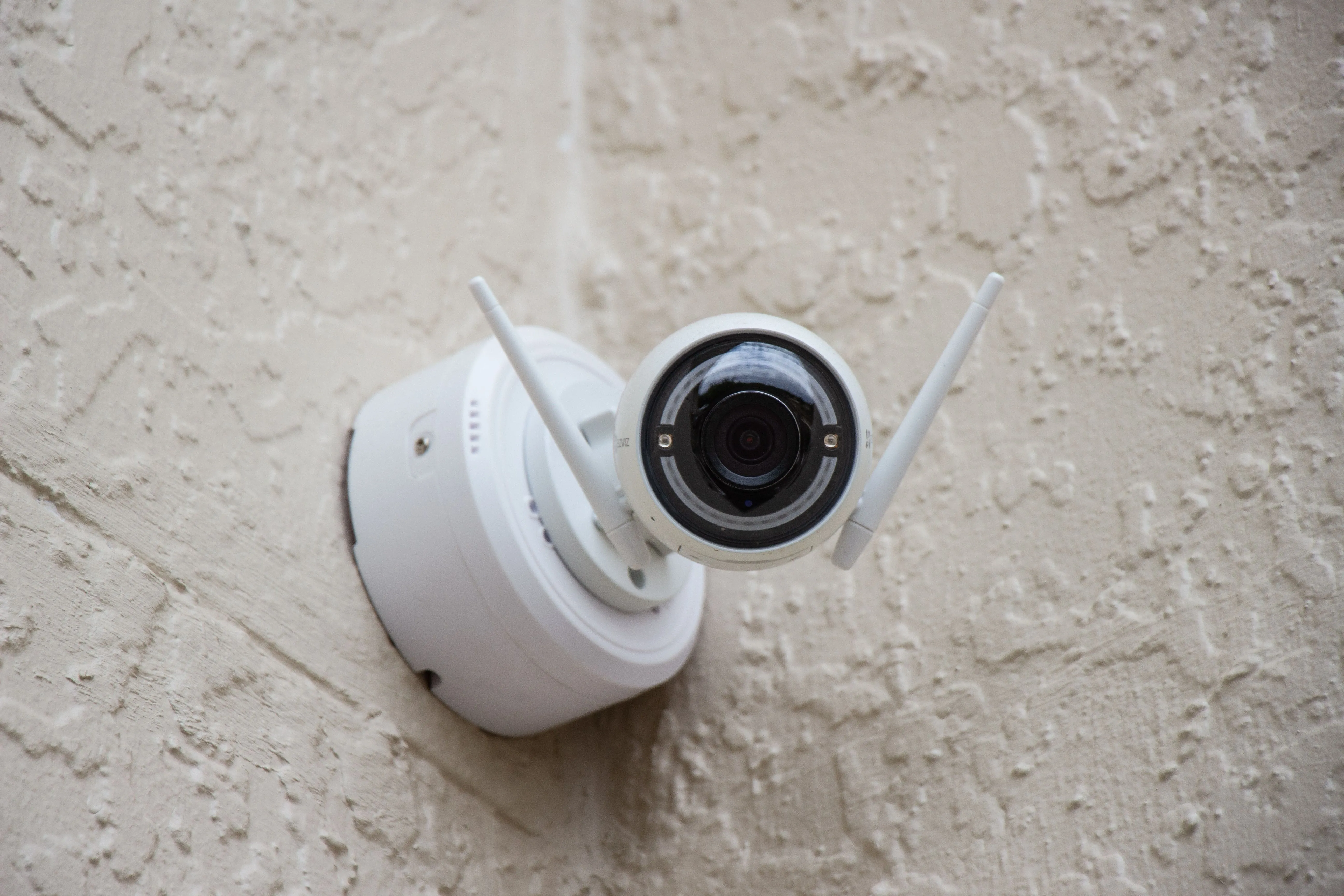 Camera an ninh không dây màu trắng gắn tường, minh họa việc truy cập hệ thống giám sát từ xa qua Port Forwarding
