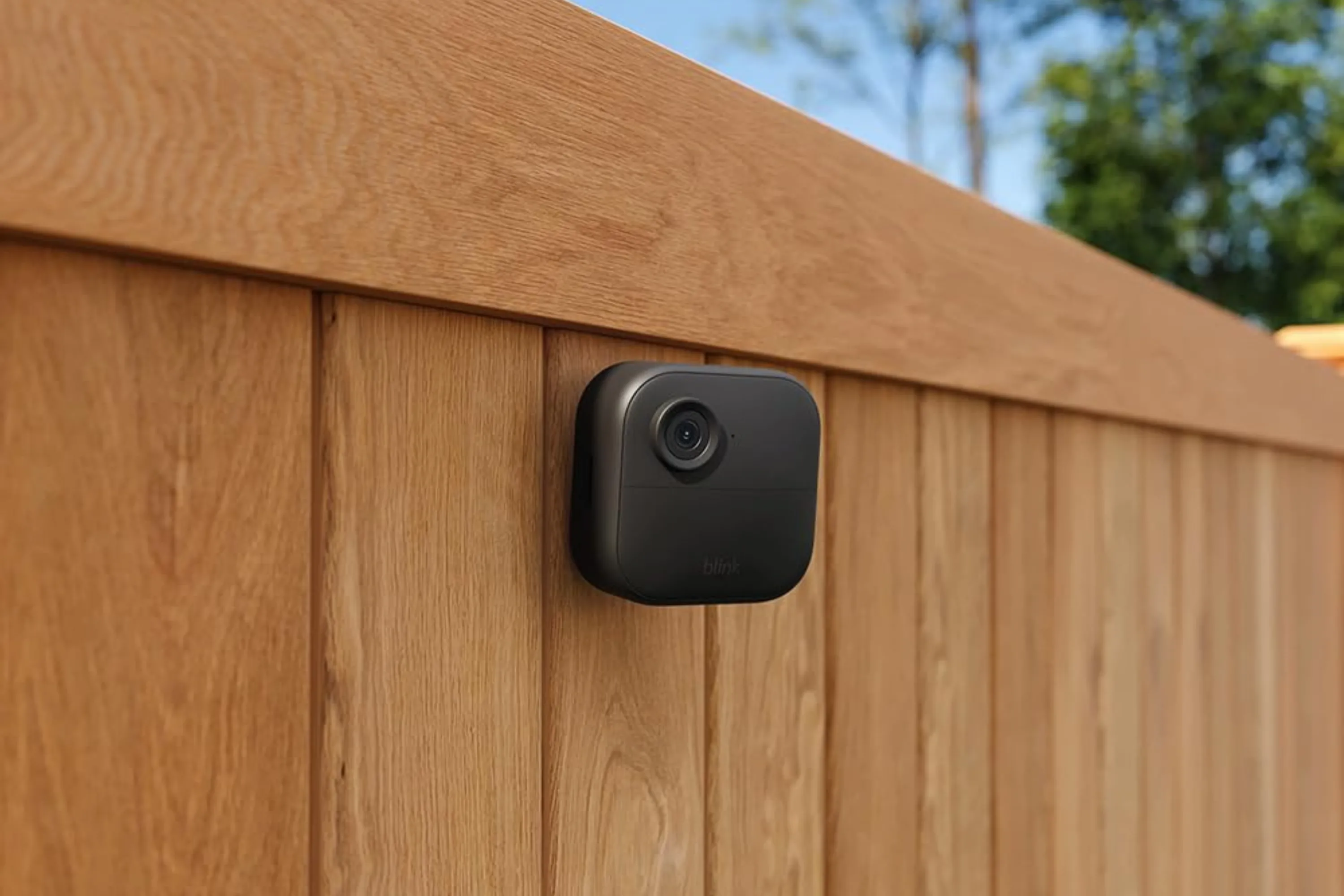 Camera Blink Outdoor 4 được lắp đặt trên hàng rào gỗ, giám sát hiệu quả khu vực sân vườn, minh họa tính năng chống chịu thời tiết.