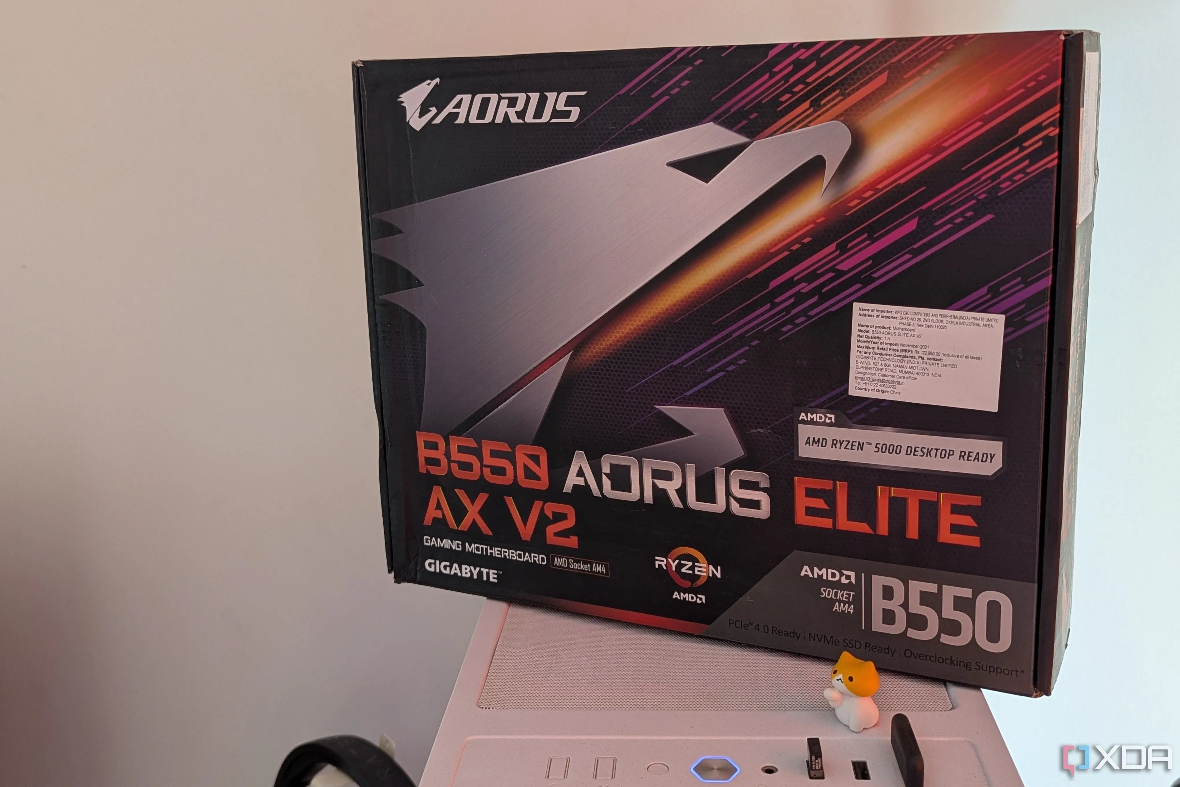 Hộp bo mạch chủ Gigabyte B550 Aorus Elite AX V2 đặt trên vỏ case PC màu trắng, minh họa tính năng RGB trên mainboard