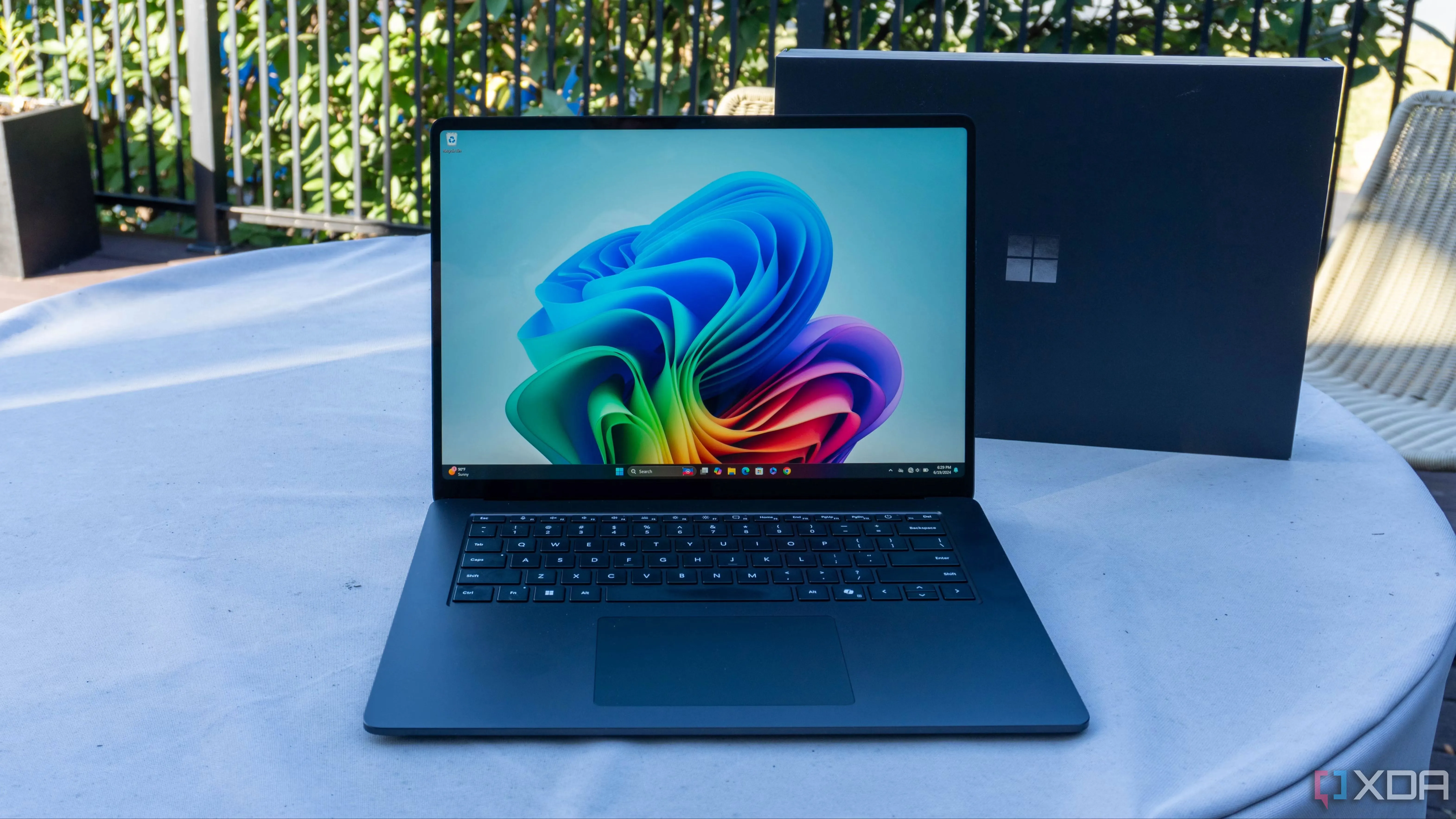Laptop Microsoft Surface Laptop 7 màu đen đặt trên bàn làm việc cùng cốc cà phê, thể hiện khả năng làm việc linh hoạt và tính di động cao.