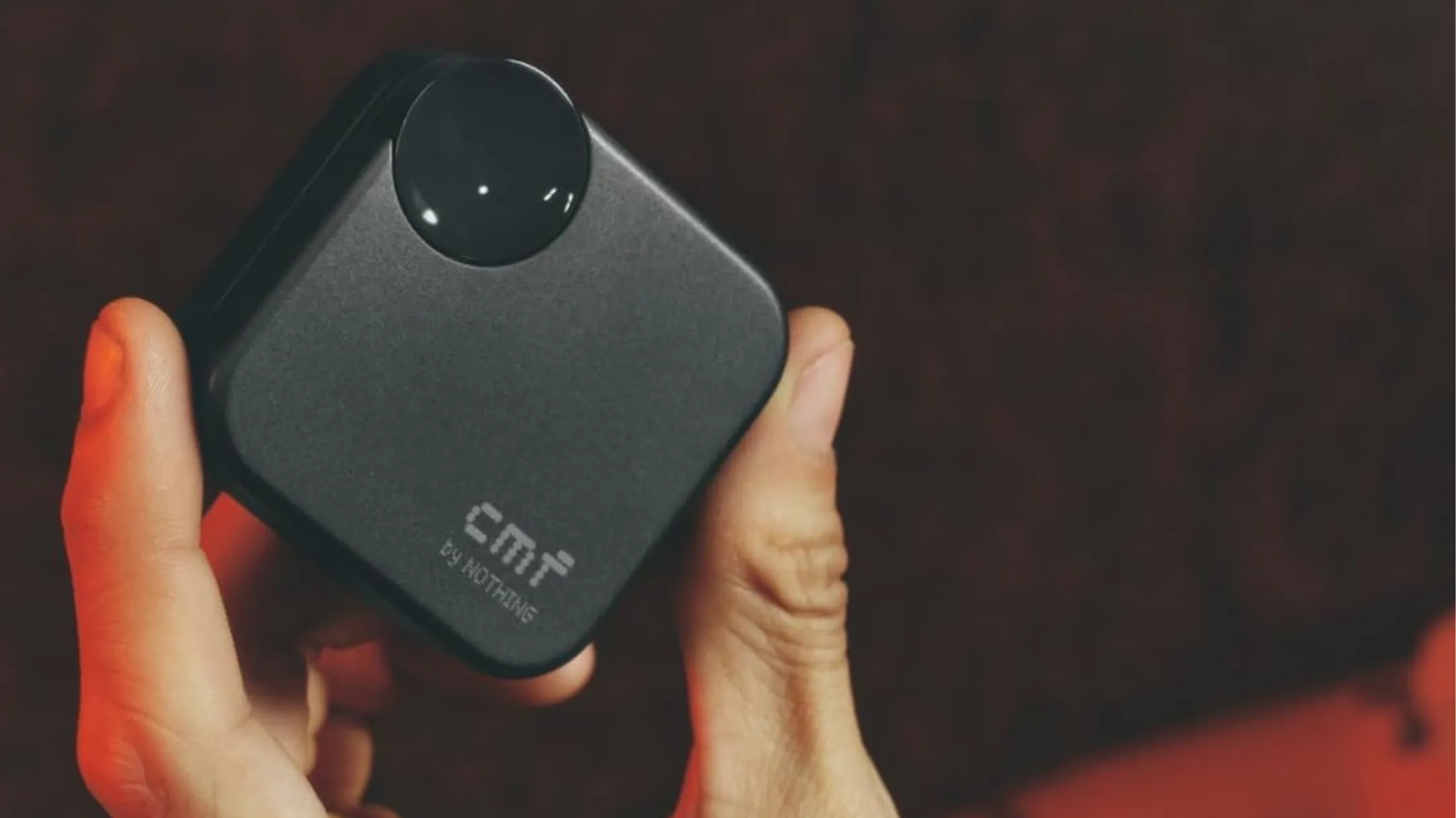 Một người đang cầm hộp sạc và tai nghe không dây CMF Buds 2a màu đen trên tay
