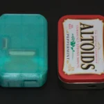 Pi Tin console cầm tay đặt cạnh vỏ hộp Altoids, minh họa kích thước nhỏ gọn của thiết bị.