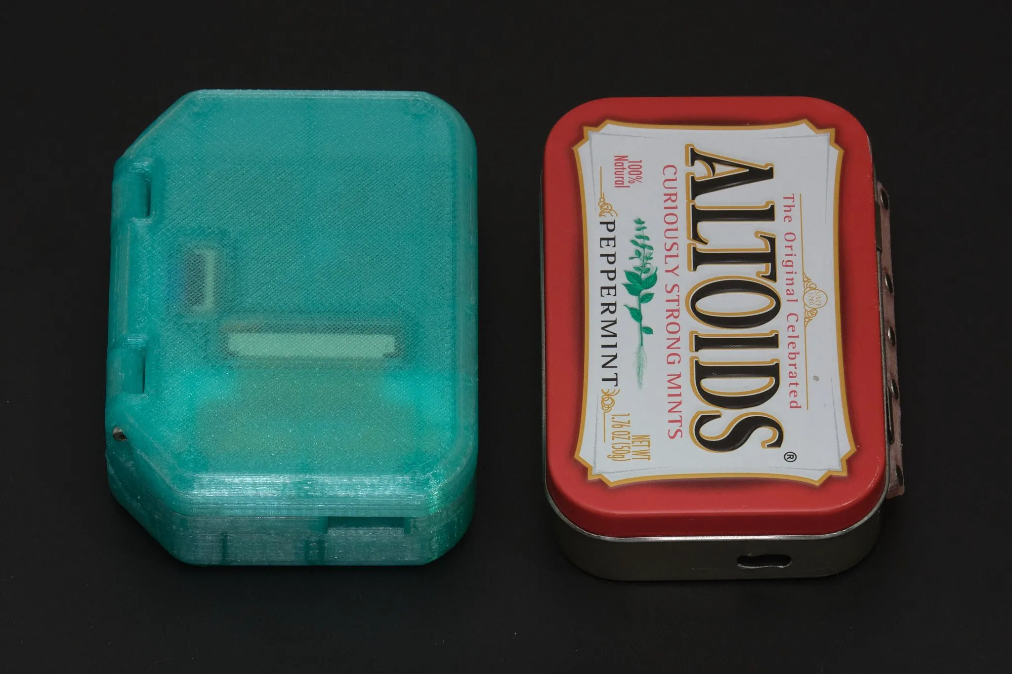Pi Tin console cầm tay đặt cạnh vỏ hộp Altoids, minh họa kích thước nhỏ gọn của thiết bị.