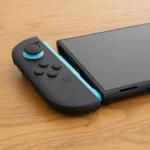 Tay cầm Joy-Con 2 màu xanh và đỏ tháo rời, đặt cạnh khe cắm tương ứng trên thân máy Nintendo Switch 2, thể hiện thiết kế module và khả năng chơi cầm tay.